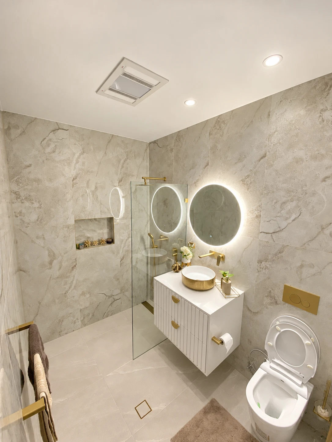 West Hoxton bathroom with pale stone tiles, illuminated round mirror, white vanity and gold fittings